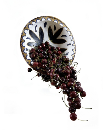 Cherries spilling from a fleur de lis bowl.